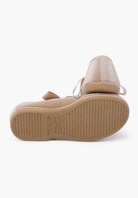 Zapatos de ante beige suave con una suela de goma texturizada, que presentan una punta redondeada y un acento de cinta en la parte trasera, diseñados para la comodidad y el estilo.