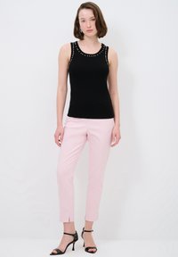 Zwarte mouwloze top met studs op de schouders, gecombineerd met lichtroze op maat gemaakte broek met enkel-splitten en zwarte hoge hakken.