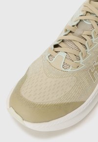 Chaussure de sport beige avec un dessus en maille texturée, un capuchon de toe lisse et des accents vert clair sur les lacets et les détails. Semelle blanche.
