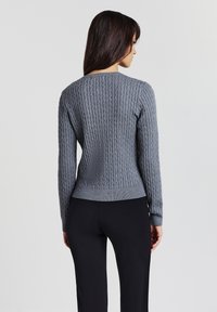 Maglione grigio lavorato a maglia con una texture a coste, maniche lunghe e una silhouette aderente. Presenta un collo rotondo e un orlo che si ferma in vita.