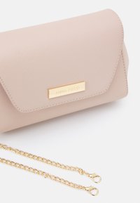 Beige clutch bag with textured material, flap closure, gold logo plate, and detachable gold chain strap. Smooth, minimalist design.