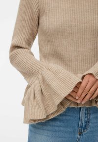 Maglione beige a costine con maniche svasate, caratterizzato da una consistenza morbida e un corpo aderente. I dettagli includono un orlo arricciato sulle maniche.
