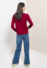 Rød langærmet skjorte, afslappet pasform, parret med lyseblå brede jeans. Neutralfarvet fodtøj afslutter outfittet.