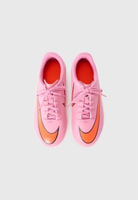 Baskets de sport roses avec une texture lisse, présentant un logo Nike en orange et un intérieur rouge. Les lacets sont roses et soigneusement attachés.