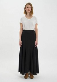 Jupe noire taille haute avec un ourlet évasé ; associée à un t-shirt blanc à col en V ample ; présentée sur un fond neutre.