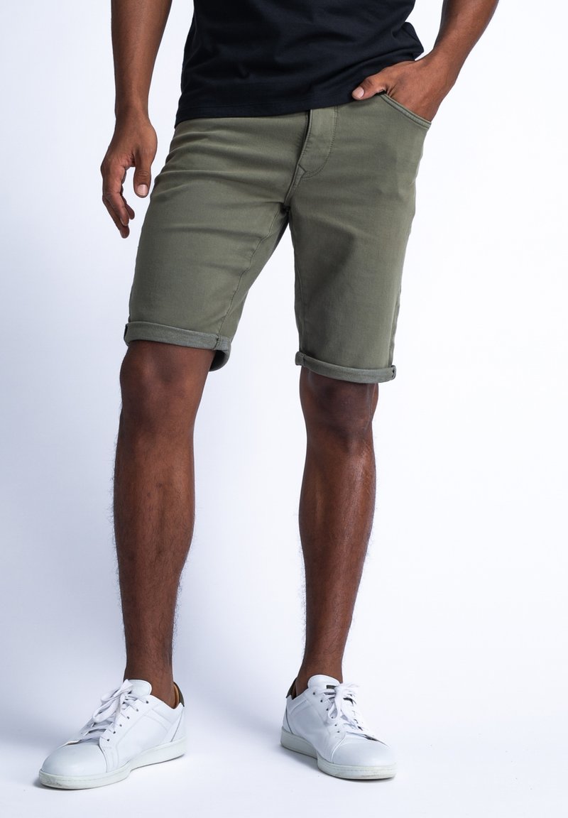 Bermudas de algodón color caqui con dobladillos enrollados, bolsillos laterales y un diseño ajustado, combinadas con zapatillas blancas que presentan acentos minimalistas.