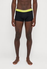 Čierne boxerské nohavičky s limetkovozeleným pásom, na ktorom je logo "Lacoste". Mäkká látka, priliehavý strih a dĺžka do polovice stehna.