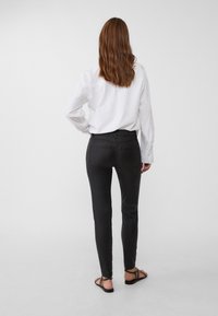 Zwarte skinny jeans met een slim fit, vijf zakken en subtiele stikdetails, gecombineerd met een witte langemouwen shirt en sandalen.