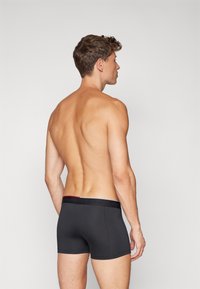 Zwarte katoenen boxershorts met een rode en zwarte patroon tailleband, die een nauwsluitende pasvorm en naadloos ontwerp hebben. Achteraanzicht weergegeven.