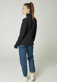 Schwarzes Langarmshirt mit hohem Kragen, kombiniert mit blauen Jeans und weißen Sneakern. Sichtbare Nähte und Details in lockerer Passform.