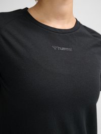 Close-up van een zwart sportshirt met ronde hals en klein ingebosseleerd hummel-logo op de borst.