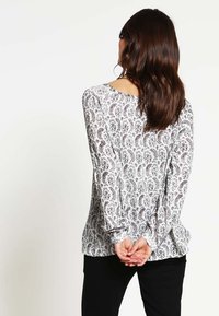 Blusa a maniche lunghe in tessuto bianco con motivo paisley in nero e bordeaux, con scollatura rotonda e vestibilità ampia.