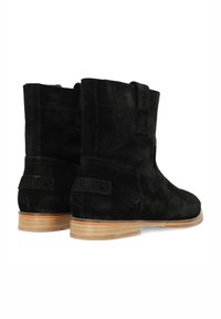 Black suede ankle boots with a smooth texture, rounded toe, and light wooden heel. Features a pull tab and embossed branding on the side.