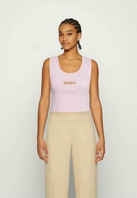 Top cropped rosa com decote arredondado, apresentando o logótipo "Kickers" em laranja na parte da frente. Textura suave, mangas curtas.