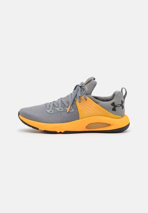 Chaussure de sport Under Armour grise et orange avec tige en mesh, fermeture à lacets, semelle intermédiaire rembourrée et logo noir au talon.