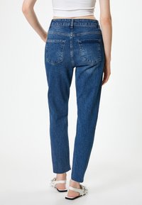 Jean en denim bleu pour homme avec un design à jambe droite, taille haute, et deux poches arrière. Le tissu a une apparence texturée et légèrement décolorée.