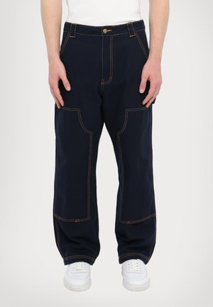 Navy blue cargo pants with contrasting orange stitching, featuring multiple pockets and a relaxed fit. Worn with white sneakers.
