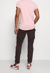 Rosa kortärmad t-shirt med rundad nederkant, kombinerad med mörkbruna cargo-byxor med sidofickor och slät textur. Kombinerad med vinröda sneakers.