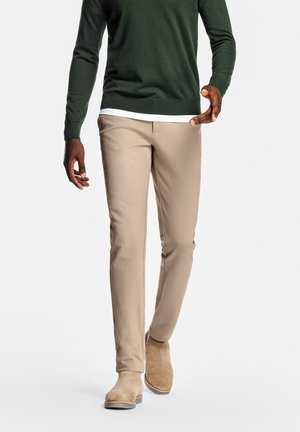 Beige Chinos im Slim-Fit, aus glattem Stoff; kombiniert mit einem grünen Pullover und hellen Wildlederstiefeln.