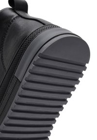 Sneaker in pelle nera con un design testurizzato, suola in gomma con scanalature orizzontali e punta arrotondata piatta.