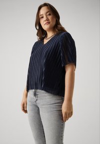 Navy pleated blouse with a V-neck and short sleeves, crafted from lightweight fabric, paired with light grey skinny jeans. Silver chain necklace accent.