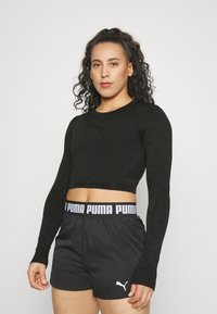Must mustriga mustardiga crop-top, millel on tekstuuriga muster ja PUMA logo, koos mustade lühikestega, millel on elastne vöökoht ja logo aktsent.