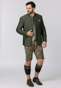 Green linen jacket with button front, paired with beige leather shorts featuring floral embroidery. Finished with knit leg warmers and brown shoes.