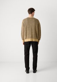 Sweter dziany w kolorze beżowym i czarnym w wzór kratki, z długimi rękawami i luźnym krojem, w połączeniu z czarnymi spodniami i butami.