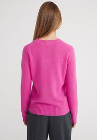 Maglione rosa a maglia con scollo rotondo, polsini e orlo a coste. Texture morbida con design aderente, visto da dietro.