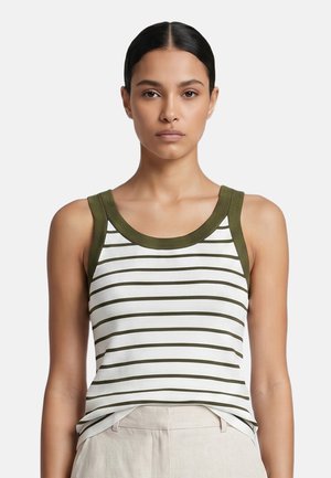 Woman with dark hair tied back wears a sleeveless white top with olive green horizontal stripes and trim, paired with light beige pants.