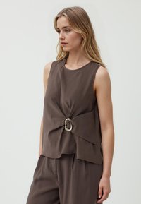 Top marrone senza maniche con scollatura rotonda, caratterizzato da una fibbia decorativa in argento in vita e un design drappeggiato e stratificato. Tessuto liscio.