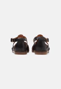 Černé kožené sandály s páskem na patě a sponou, které mají výřezové detaily a hnědou podrážku. Hladká textura a minimální designové prvky.