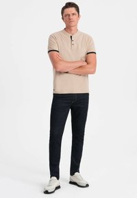 Béžové polo tričko s krátkým rukávem a černými akcenty, s knoflíkovou légou, v kombinaci s tmavými džíny a světlými botami. Jednoduchý design a přiléhavý střih.