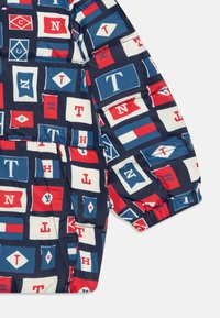 Kurtka puchowa w granatowe, czerwone i białe geometryczne wzory z różnymi projektami flag. Wykonana z błyszczącego materiału z elastycznymi mankietami.