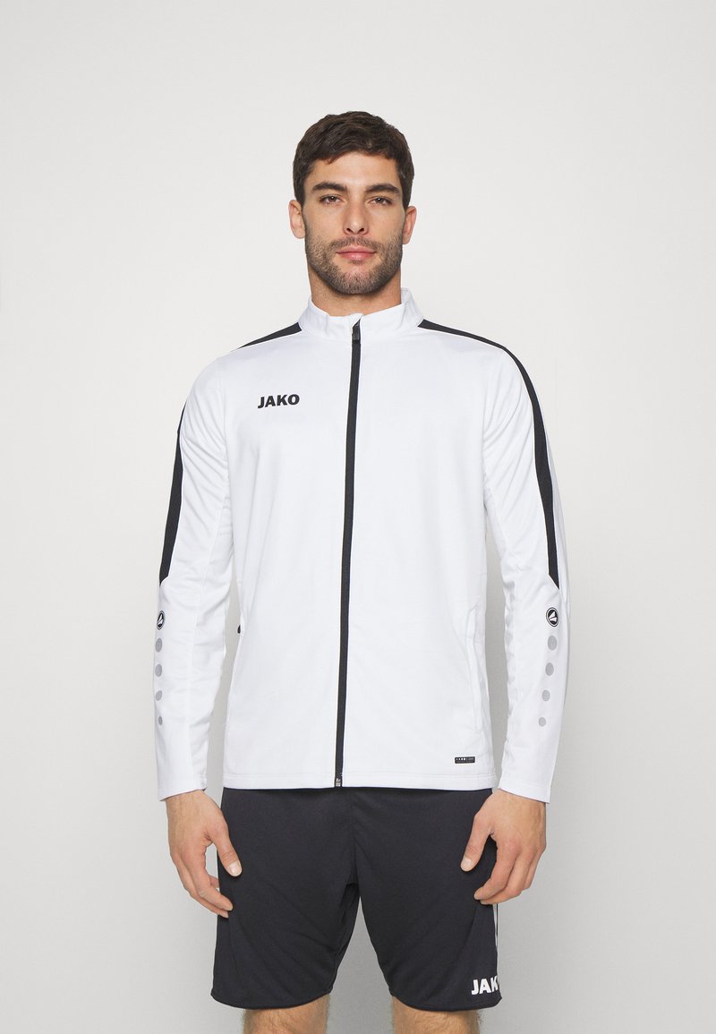 Witte sportjack met zwarte accenten, volledige rits, hoge kraag en JAKO-logo. Bevat knoopdetails op de mouwen en een gladde, lichte stof.