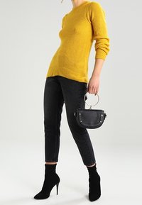Mustard-yellow ribbed sweater, black high-waisted jeans, black stiletto ankle boots, and small black handbag with a circular handle.