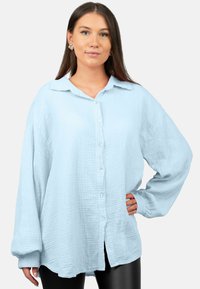 Chemise bleu clair à boutons, fabriquée en tissu texturé, avec un col, des manches longues et une coupe ample avec un ourlet arrondi.