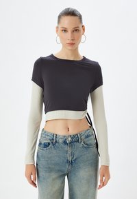 Korte top met korte donkergrey ribgebreide mouwen en een lichtgrijs lange mouwlaag, met een zijstrikdetail. Gemaakt in combinatie met high-waisted jeans.