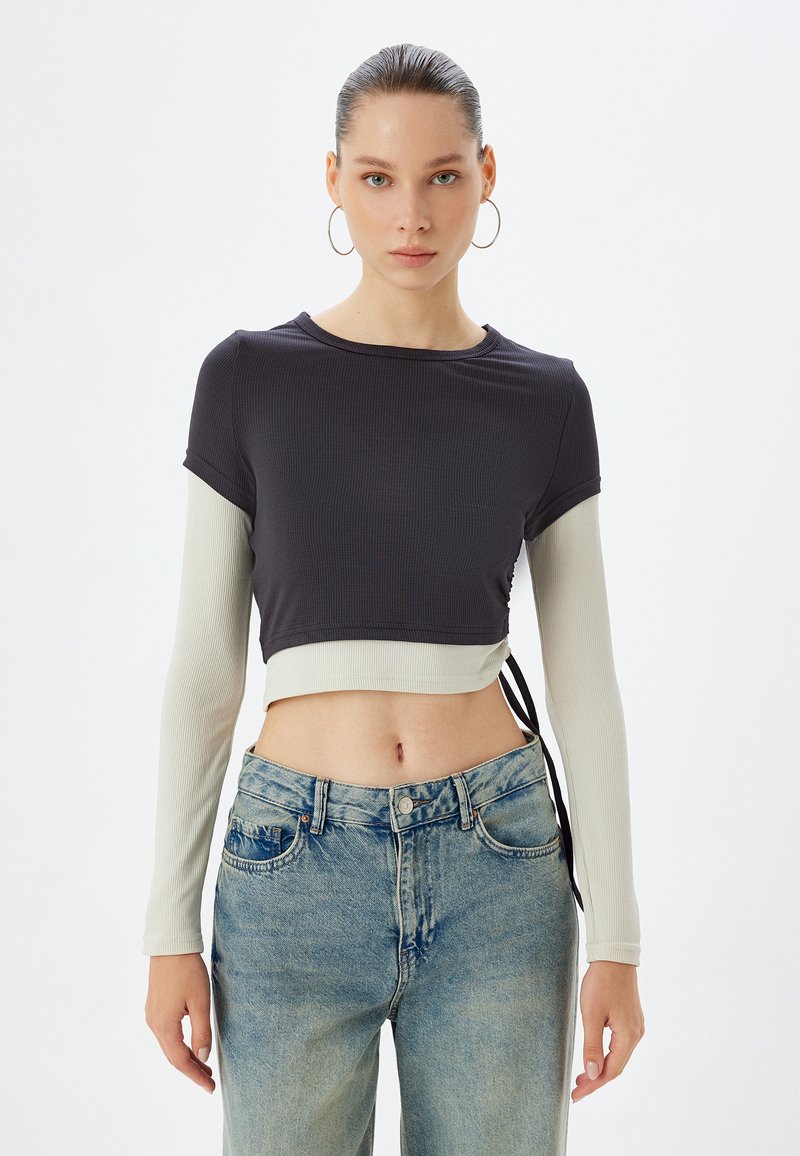 Korte top met korte donkergrey ribgebreide mouwen en een lichtgrijs lange mouwlaag, met een zijstrikdetail. Gemaakt in combinatie met high-waisted jeans.