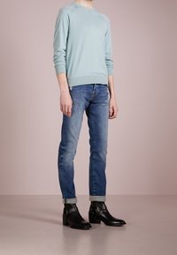 Světle modrý svetr s dlouhými rukávy, kombinovaný s vybledlými modrými džíny s ohrnutými manžetami. Černé kotníkové boty se šňůrkami a hladkým povrchem.