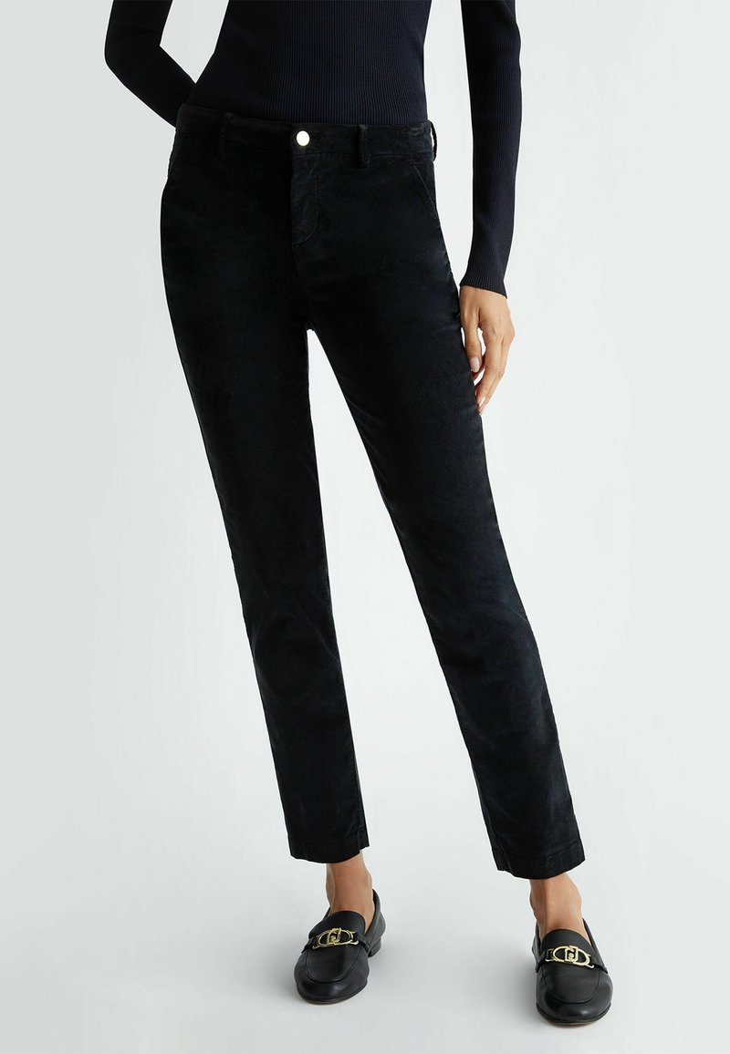 Pantaloni in corduroy neri con una vestibilità slim, forma dritta, tasche frontali e chiusura con bottone. Texture morbida con una leggera lucentezza.