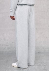 Pantalones de chándal gris claro hechos de algodón suave, con un corte holgado, bolsillos laterales y cintura elástica, combinados con zapatillas blancas.
