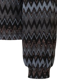 Schwarz-grauer Strickstoff mit Zickzackmustern und dezenten metallischen Akzenten. Die Manschette ist elastisch für eine enganliegende Passform.