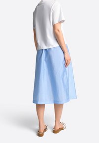Falda azul clara en forma de A con una textura suave y brillante, combinada con una blusa blanca de manga corta. El calzado presenta una suela de madera marrón y correas.
