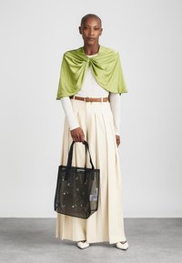 Grøn satin kappe over en hvid langærmet top, beige plisseret nederdel og en sort nettaske med blomsterudsmykninger. Hvide spidse sko.