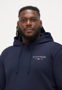 Ναυρίσι μπλουζάκι με κουκούλα από μαλακό ύφασμα. Διαθέτει το λογότυπο "HILFIGER" με κόκκινες, λευκές και μπλε λεπτομέρειες. Χορδές στην κουκούλα.