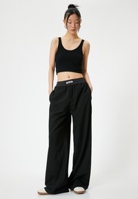 Zwarte geribde crop top en losse zwarte broek met een elastische tailleband. Opvallende details zijn een logo op de tailleband en zijzakken.