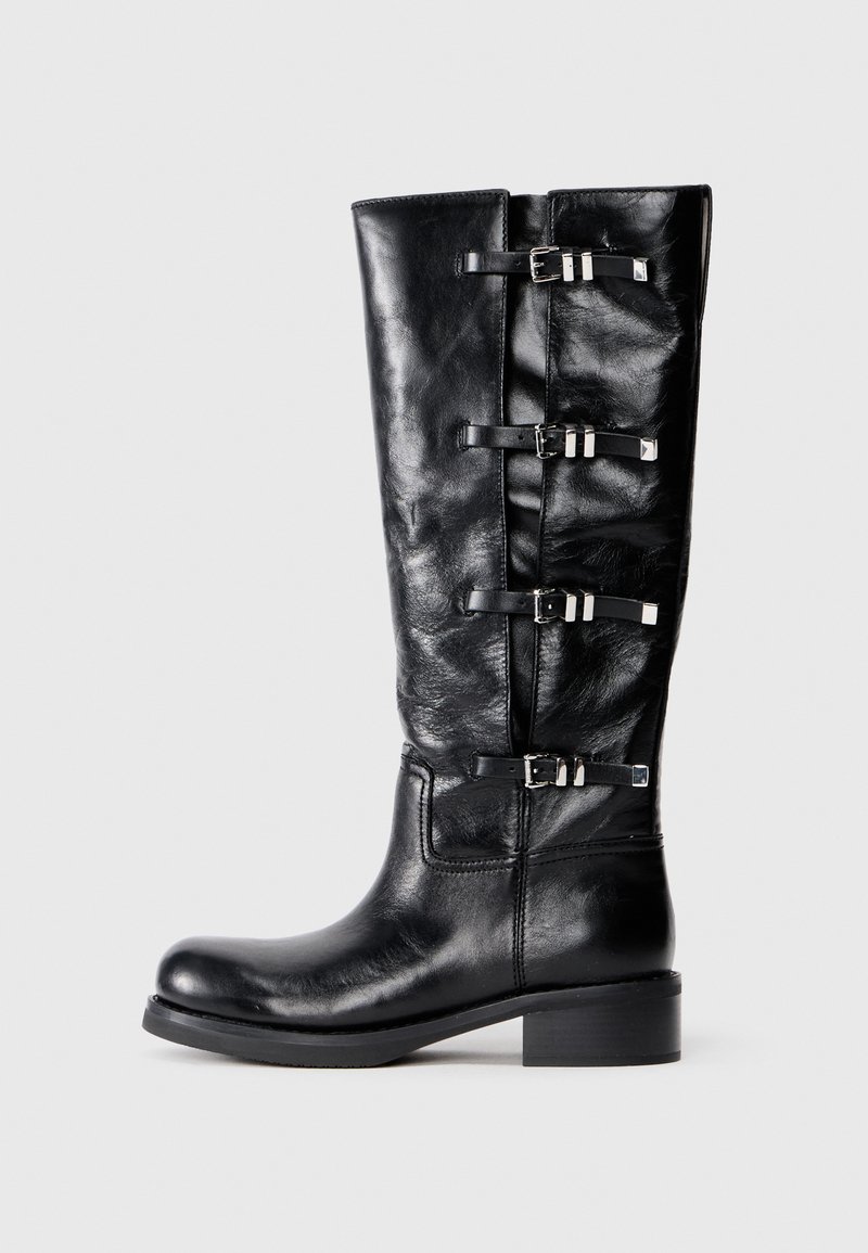 Bottines en cuir noir, hauteur genou, avec un bout arrondi, présentant trois accents de sangle avec des boucles en métal et un petit talon carré. Texture lisse.