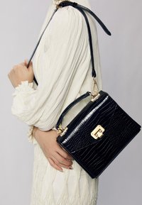 Svart läderhandväska med krokodilprägling och en guldfärgad låsdetalj, med ett kort handtag och en lång justerbar axelrem.