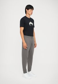 Schwarzes Baumwoll-T-Shirt mit grafischem Design und grauen Jogginghosen. Die Jogginghosen haben einen elastischen Bund und Bündchen, kombiniert mit weißen Sneakers.